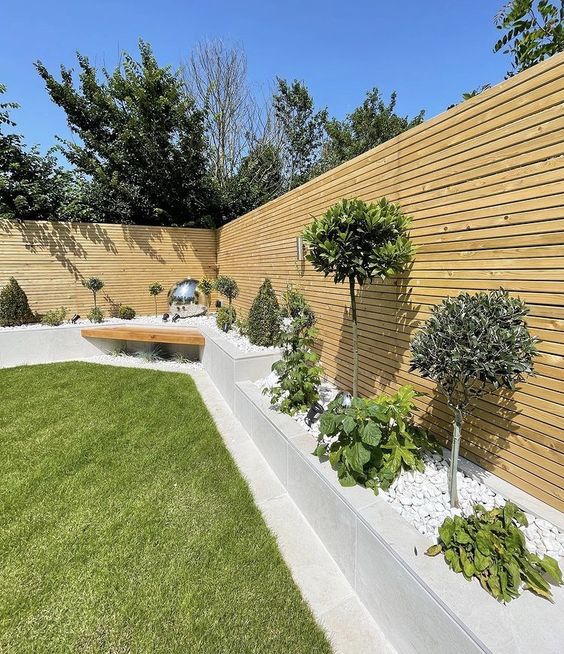 a modern garden with a green lawn, raised garden beds with greenery and stained privacy screens is cool
