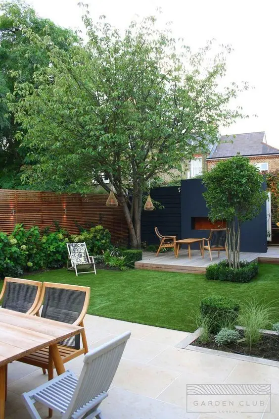 a modern garden with stained privacy screens, a green lawn and greenery, some trees and modern furniture on the deck