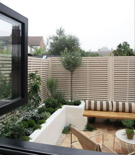 a modern outdoor space with a brick floor, stained and leather furniture, a raised bed with greenery and shutter screens