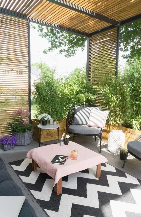 a modern pergola with a chevron rug, modern furniture, blooms and greenery plus stained privacy screens