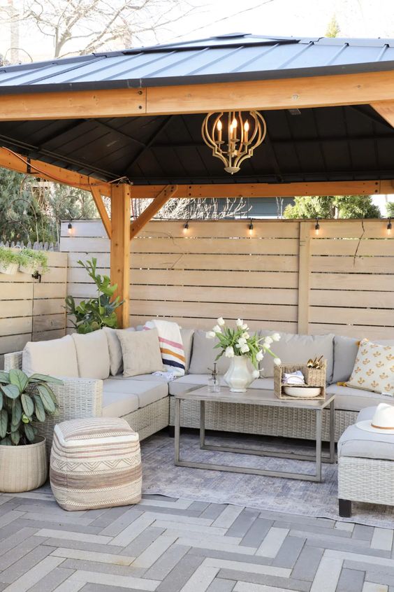 a modern pergola with privacy screens, wicker furniture, a coffee table, blooms and greenery and a boho pouf