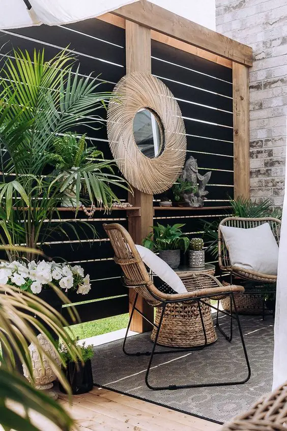 a modern terrace with a black privacy screen, rattan furniture, a side table, potted plants, a mirror and a boho printed rug