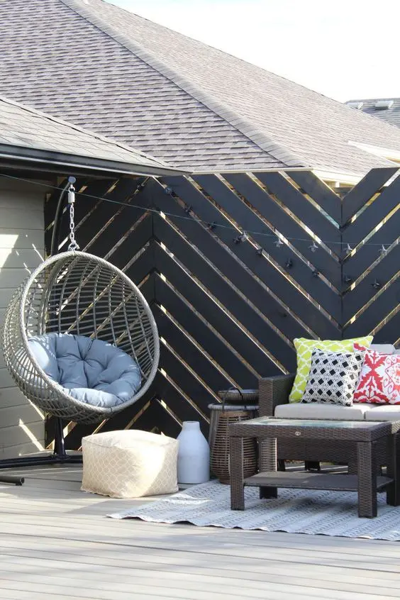a modern terrace with a hanging chair, wicker furniture, colorful pillows, a black chevron screen, lights and a boho rug