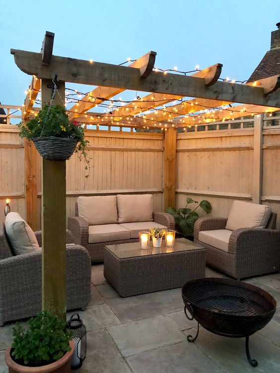 a modern terrace with privacy fence around, wicker furniture, lights, potted greenery and a fire pit