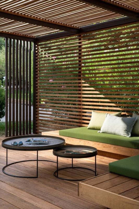 a modern terrace with privacy screens, a built-in sofa with pillows, coffee tables and greenery around