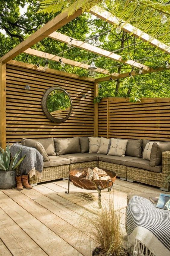 a modern terrace with privacy screens, wicker furniture, a fire pit, potted plants and a mirror plus lights over the space
