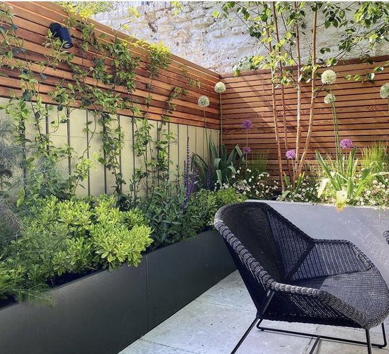 a modern terrace with stained fences and privacy screens, black planters with greenery and blooms and black garden furniture