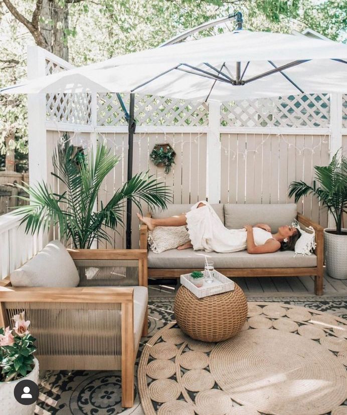 a modern tropical terrace with privacy screens, stained furniture, boho rugs, a pouf, planters with statement plants