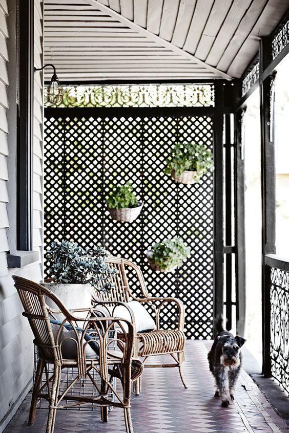 a porch with a cool privacy screen with planters attached, rattan furniture, some greenery and pillows