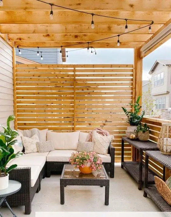 a small modern terrace with a privary screen, wicker furniture, potted plants and lights over the whole space