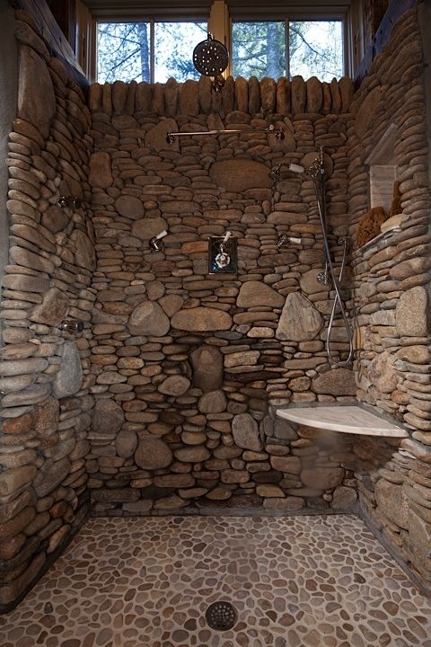a stone clad shower with a pebble tile floor looks rustic and cool