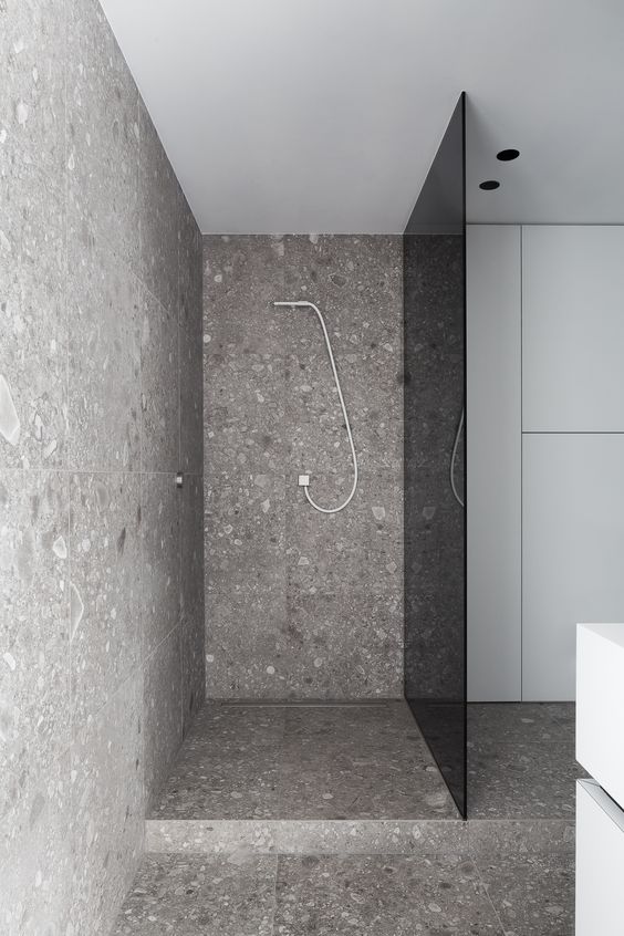a modern grey bathroom clad with terrazzo and a smoked glass shower door for privacy