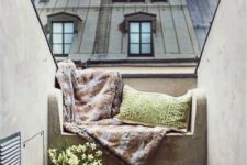 04 a concrete bench covered with blankets, pillows and cushions and potted flowers