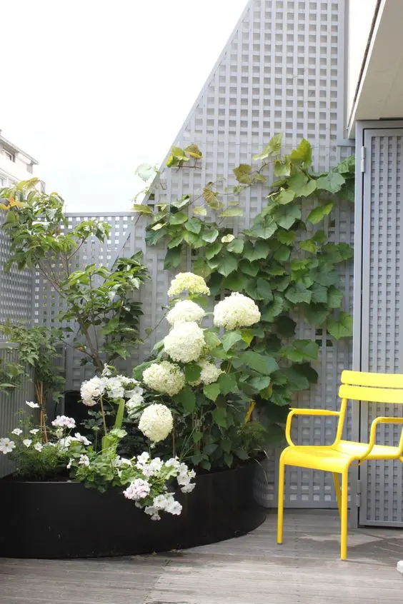 a balcony with a corner garden bed with blooms and greenery looks unusual, eye-catchy and chic