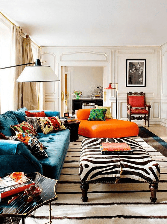 a bold living room with a turquoise sofa, colorful pillows, an orange daybed, an animal print ottoman, a striped rug and a red refined chair