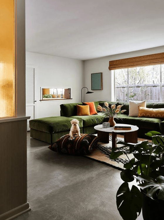 a bright and chic living room with a concrete floor, a green secitonal with bright pillows, a jute rug, a coffee table and decor