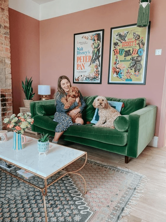 a bright living room with pink walls, a green velvet sofa, a chic coffee table and layered printed rugs plus a mini gallery wall
