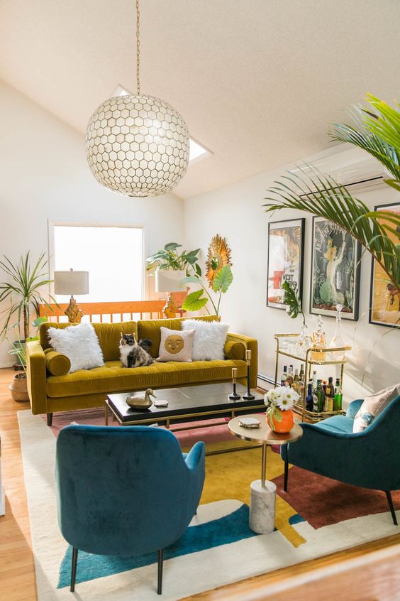 a bright modern living room with a mustard velvet sofa, navy velvet chairs, a bright rug and gallery wall plus potted plants