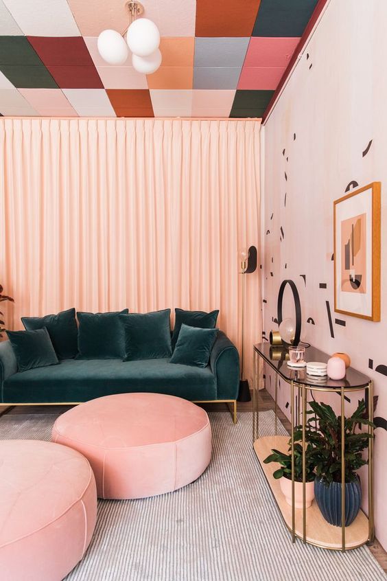 a chic modern living room with a colorful ceiling, a dark green velvet sofa and pink ottomans, a console table, a printed accent wall and some art