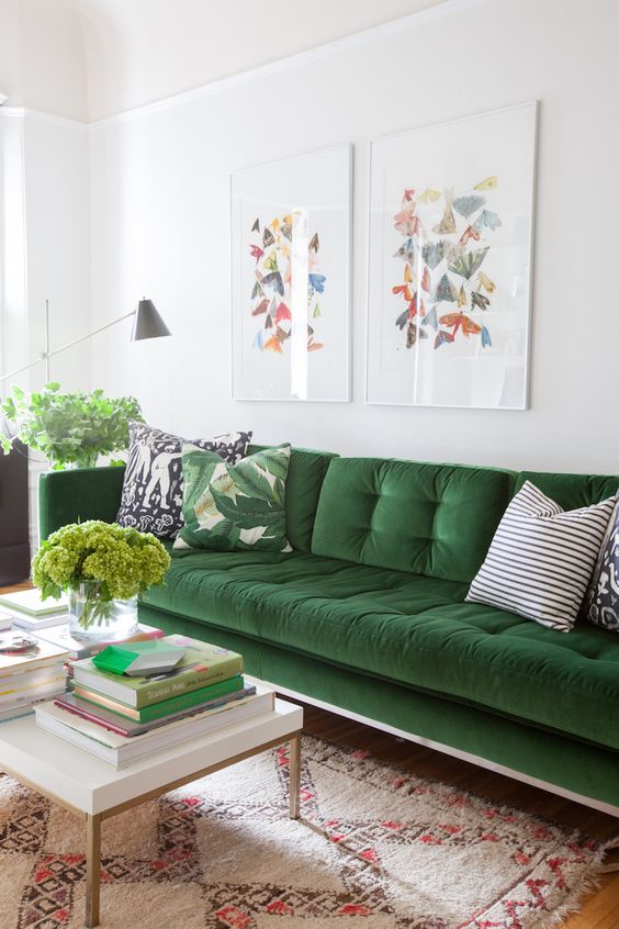 a chic neutral living room with a green velvet sofa and pillows, a boho rug, a coffee table with books, artwork, greenery and a lamp