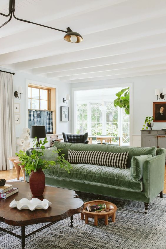a farmhouse living room with a green velvet sofa with pillows, a living edge coffee table, a neutral rug and some potted greenery