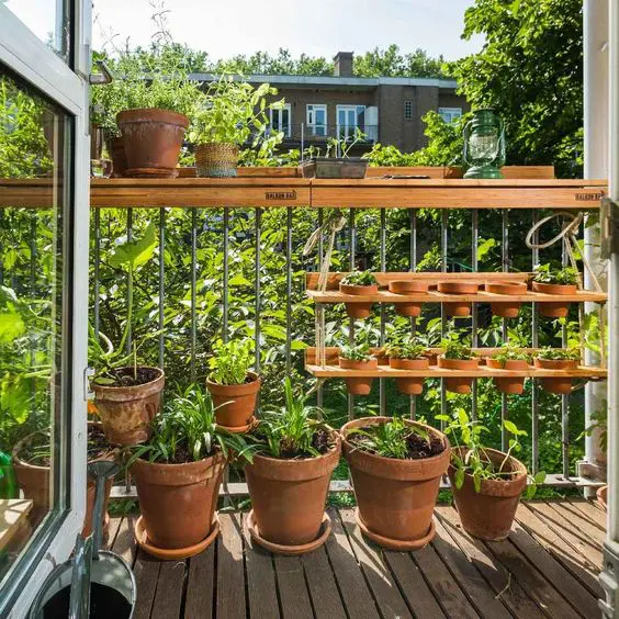 a hanging shelf with planters, some planters on the floor and railings turn a balcony into a small garden