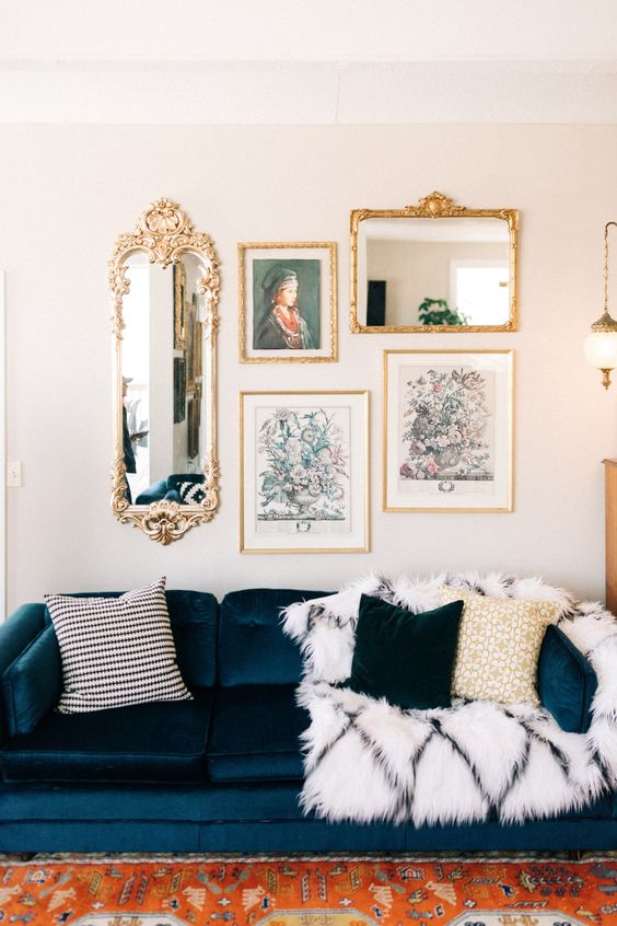 a living room with a navy velvet sofa and pillows, a pretty gallery wall with gold frames and a bold rug