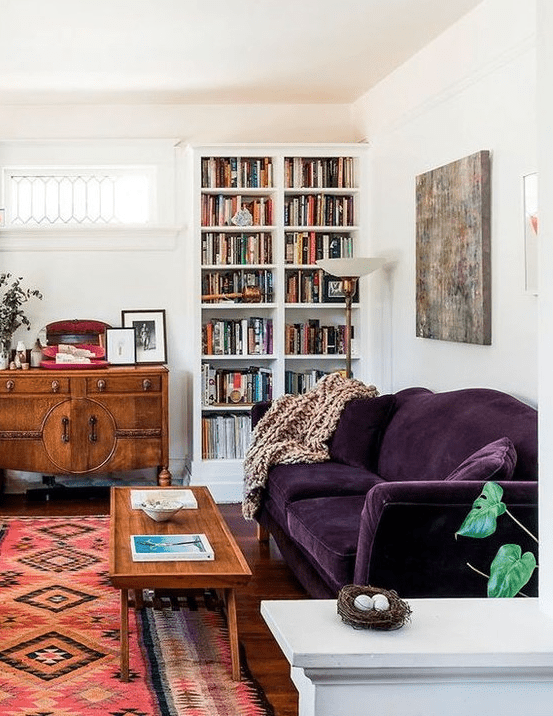 a mid-century modern living room done in neutrals and filled with color - a printed rug, a deep purple sofa, stained furniture and a built-in bookcase