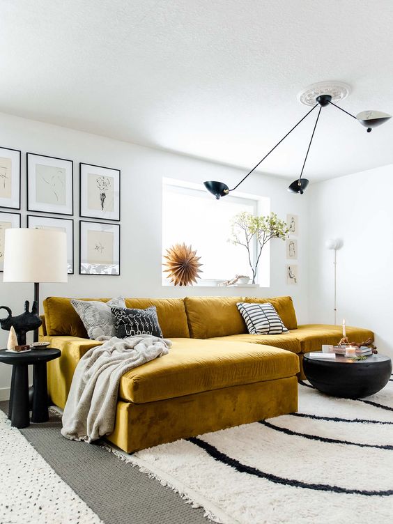 a modern living room with a mustard velvet sofa, a printed rug, a black coffee table, a ceiling lamp and a grid gallery wall
