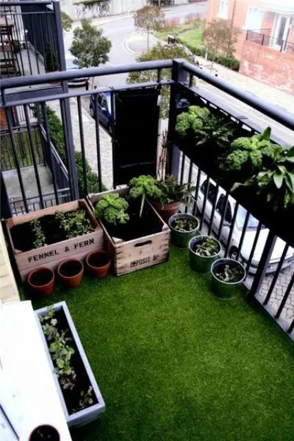 a small balcony with a railing planter and some smaller ones and crates on the floor is a cool and green space