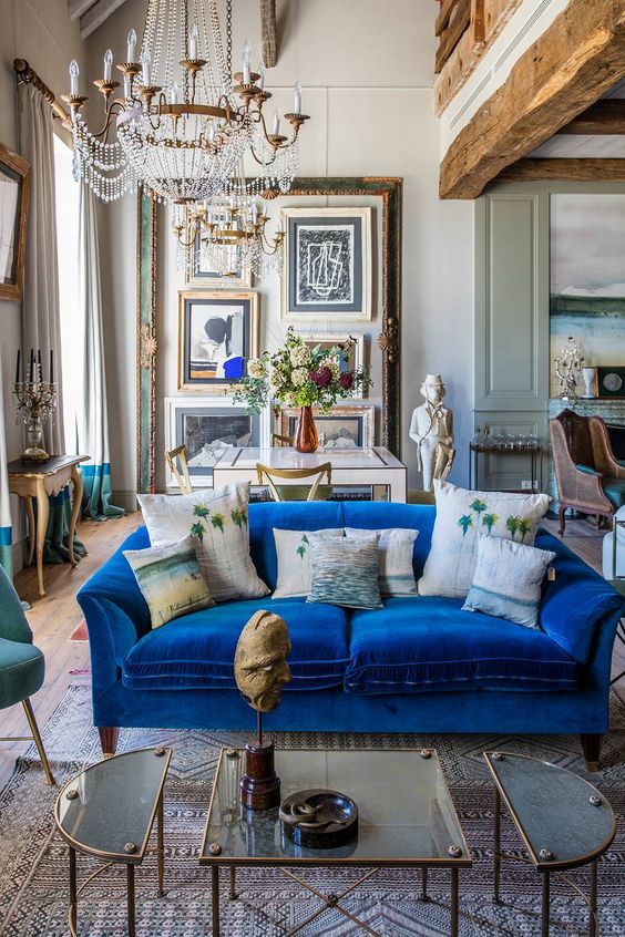 a sophisticated eclectic living room with a gallery wall, a blue velvet sofa, a coffee table of three parts, a crystal chandelier and a dining zone
