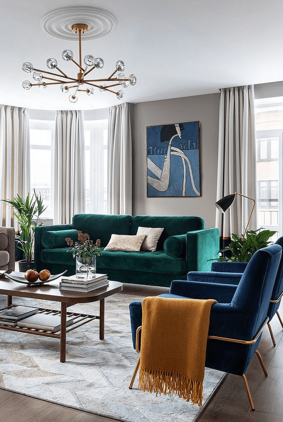a super bright living room with grey walls, a bold green sofa, navy chairs, a coffee table, a chandelier and some decor