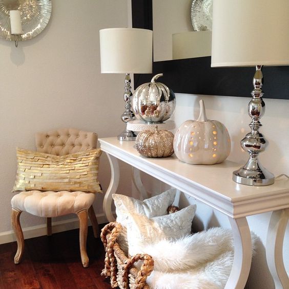 a console table with various shiny pumpkins and a wicker basket with pillows and faux fur