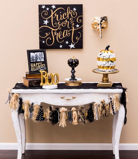 a chic cake table with glam black and gold pumpkins, a pallet sign and a cool garland