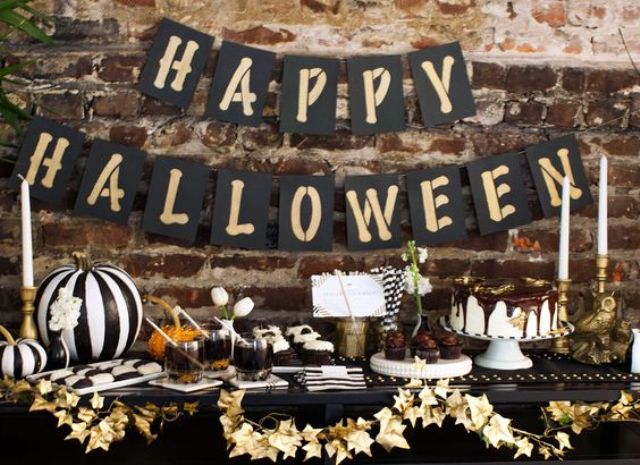 a stylish black and gold Halloween dessert table, lots of desserts and a gold leaf garland