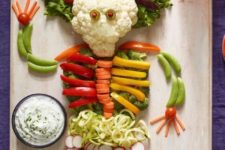 17 a veggie tray styled as a spooky human or skeleton and some dip next to it