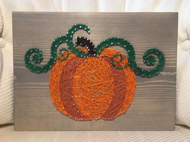 a creative pumpkin string art piece with two shades of orange and green leaves