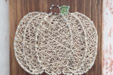 06 a neutral string art pumpkin with a gree and brown stem on a wooden board