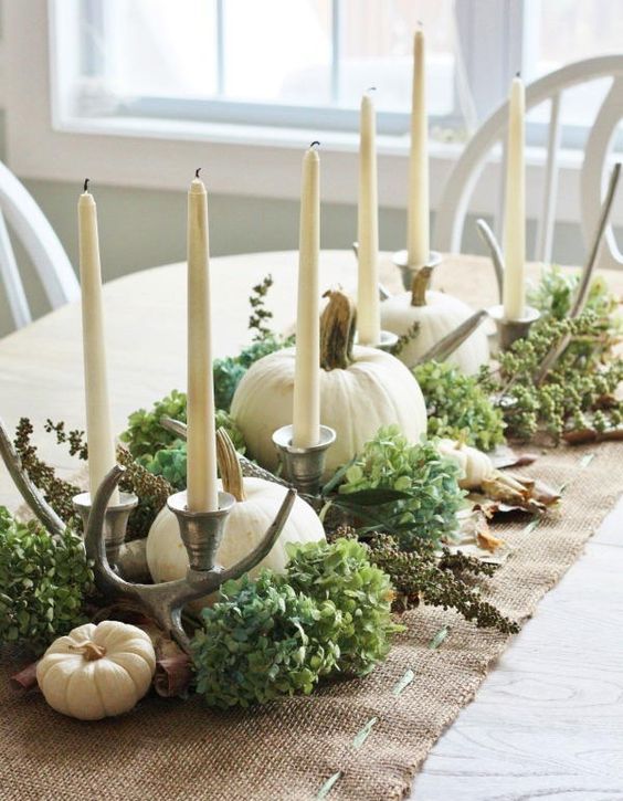 a table runner of burlap with hydrangeas, candles, pumpkins and antlers