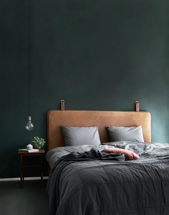 a moody bedroom with dark green walls and a brown leather headboard for a man