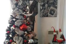 a black Christmas tree with striped ribbons, gold, silver, red and black ornaments and a Jack Skellington figure next to it