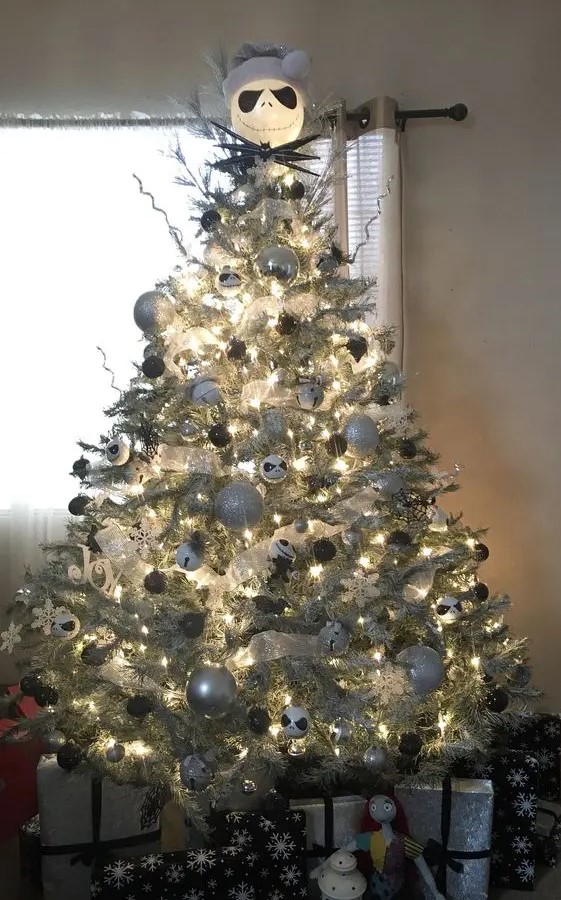 a lit up silver Christmas tree with silver, black and white ornaments, bells and a Jack Skellington head on top