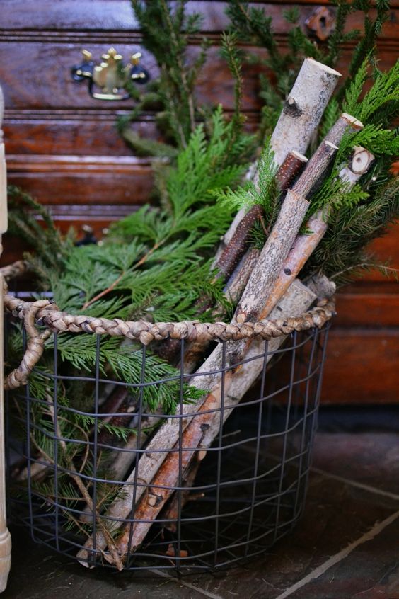 a metal basket with branches and evergrens for decorating a porch