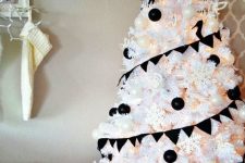 a white Christmas tree decorated with black and white ornaments, with snowflakes and lights plus a clear snowflake topper