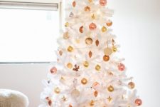a white Christmas tree decorated with gold and pink ornaments and a large gold bow on top