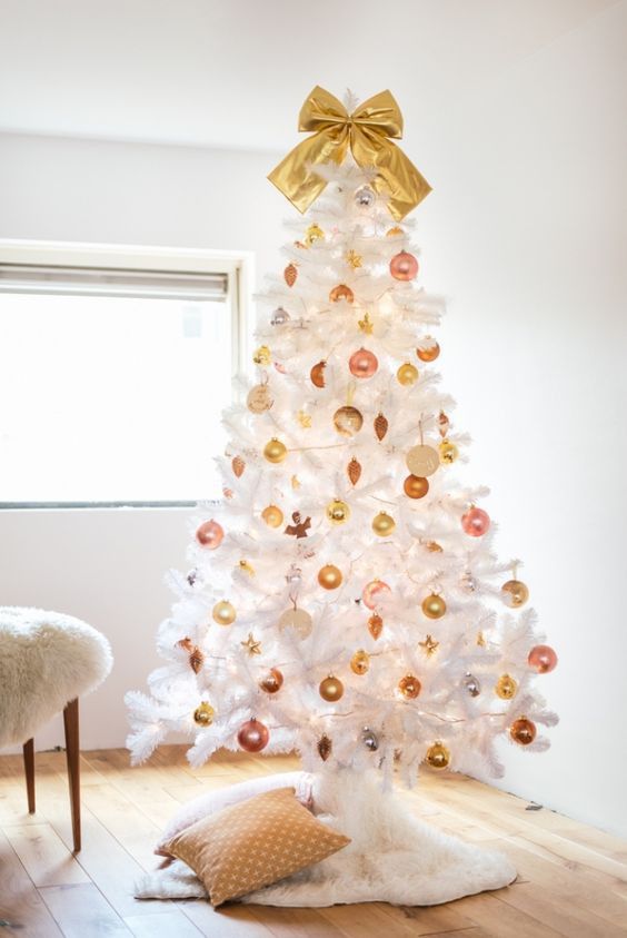 a white Christmas tree decorated with gold and pink ornaments and a large gold bow on top
