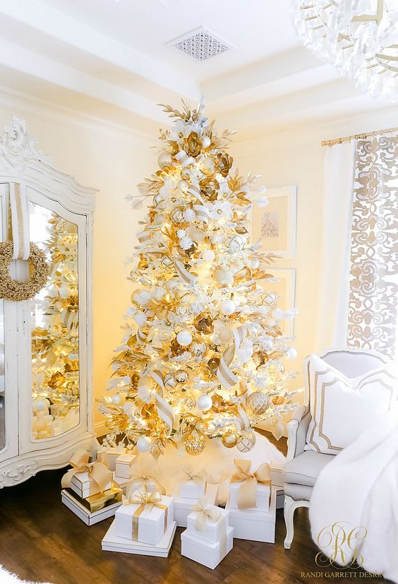 a white Christmas tree decorated with gold and white ornaments, faux blooms and leaves and lights