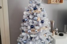 a white Christmas tree with blue, silver and navy ornaments and ribbons is a cool and catchy solution for a coastal space