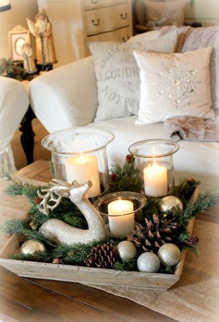 a wooden tray with pinecones, sivler ornaments, evergreens, candles and a deer figurine