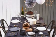 05 a simple table setting with a black tablecloth, gold stars and star-shaped garlands and signs next to it